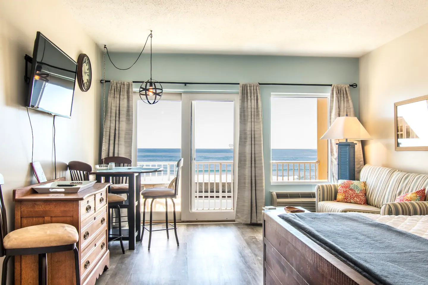 Interior of a home with large doors (featuring tall windows) that look out to the ocean. A table and chairs sits to the left. To the right is a seating area.