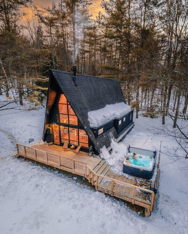 A mountain chalet in the snowy woods at dusk with interior lights on