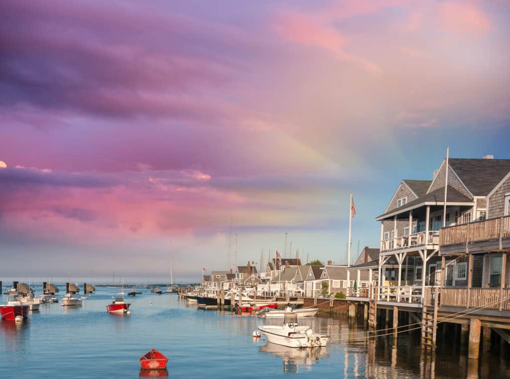 Homes along the coast under a purple and blue sky. Boats float on the water in Massachusetts.