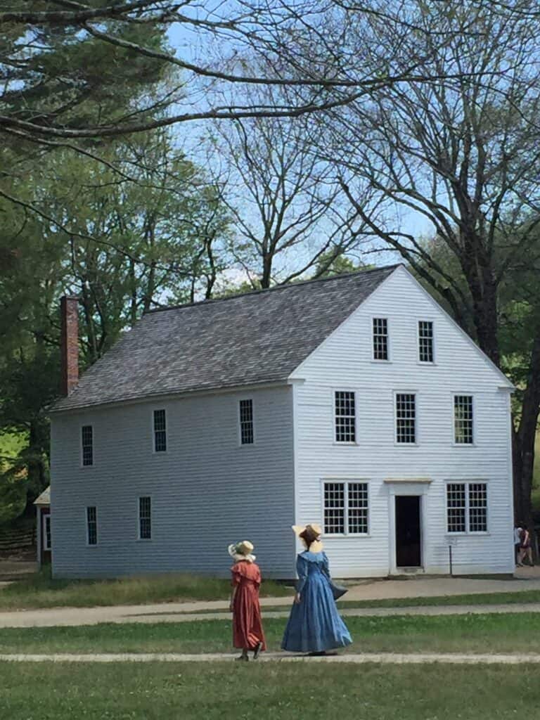 White historic home with a brick chimney. Two people with historic homes walk in front of it in Massachusetts.