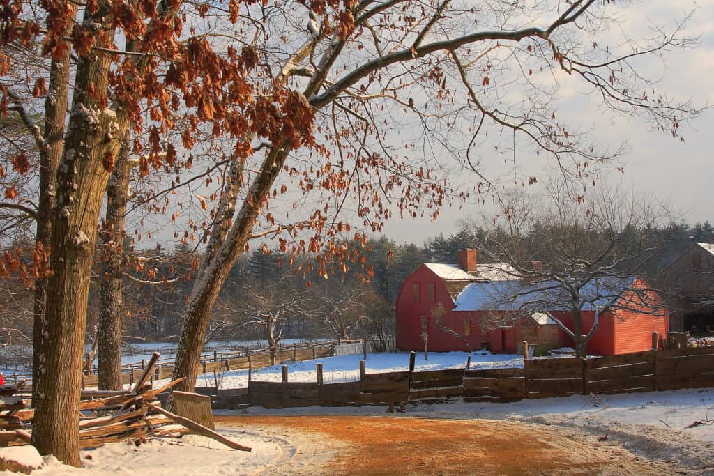 Red barn on a farm with snow. Fall foliage is hanging off trees in Massachusetts.