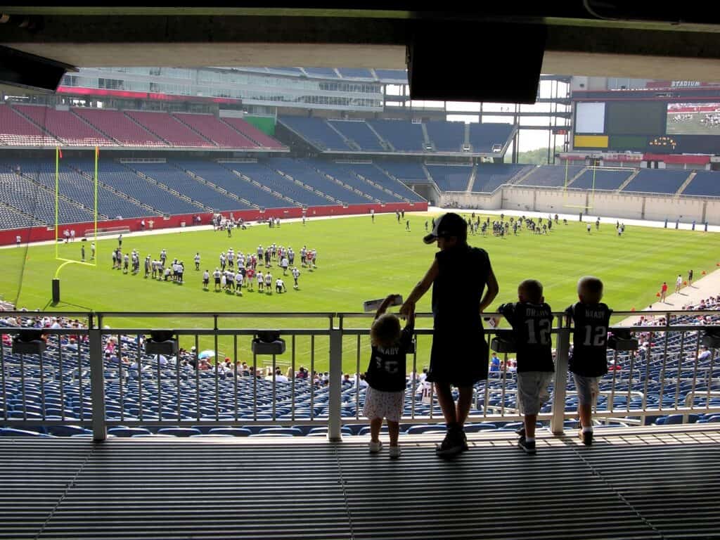 Four young children watch football practice on a field in Massachusetts.