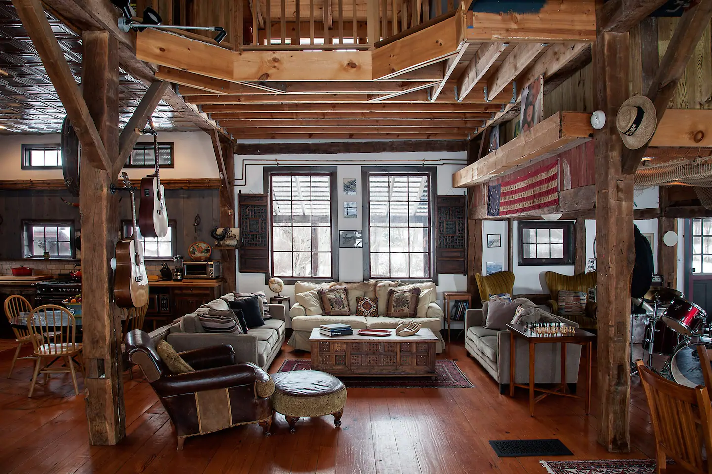 Interior of a log cabin with two floors. The bottom floor is a living room with plush grey and white couches set up around a coffee table. The top floor is a loft.