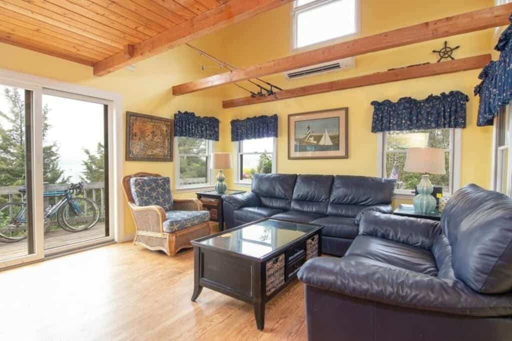 A living room with blue/grey leather couch and loveseat, with blue valances on 3 windows. 