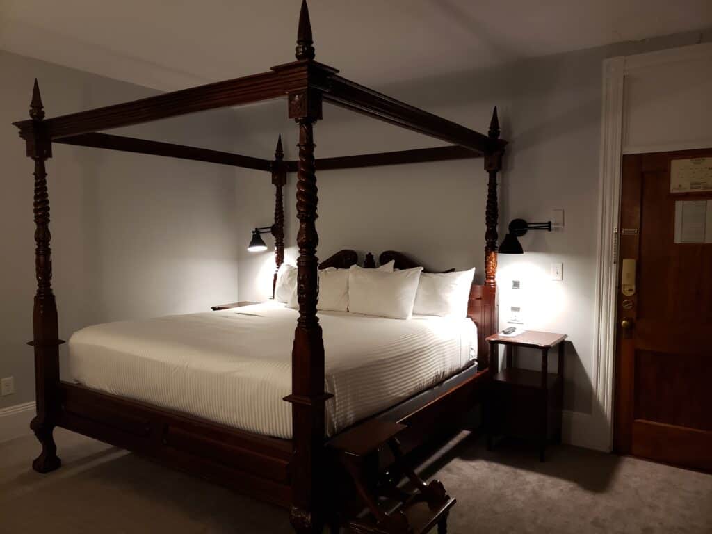Interior of a bedroom with a historic wooden canopy bed with white bedding.
