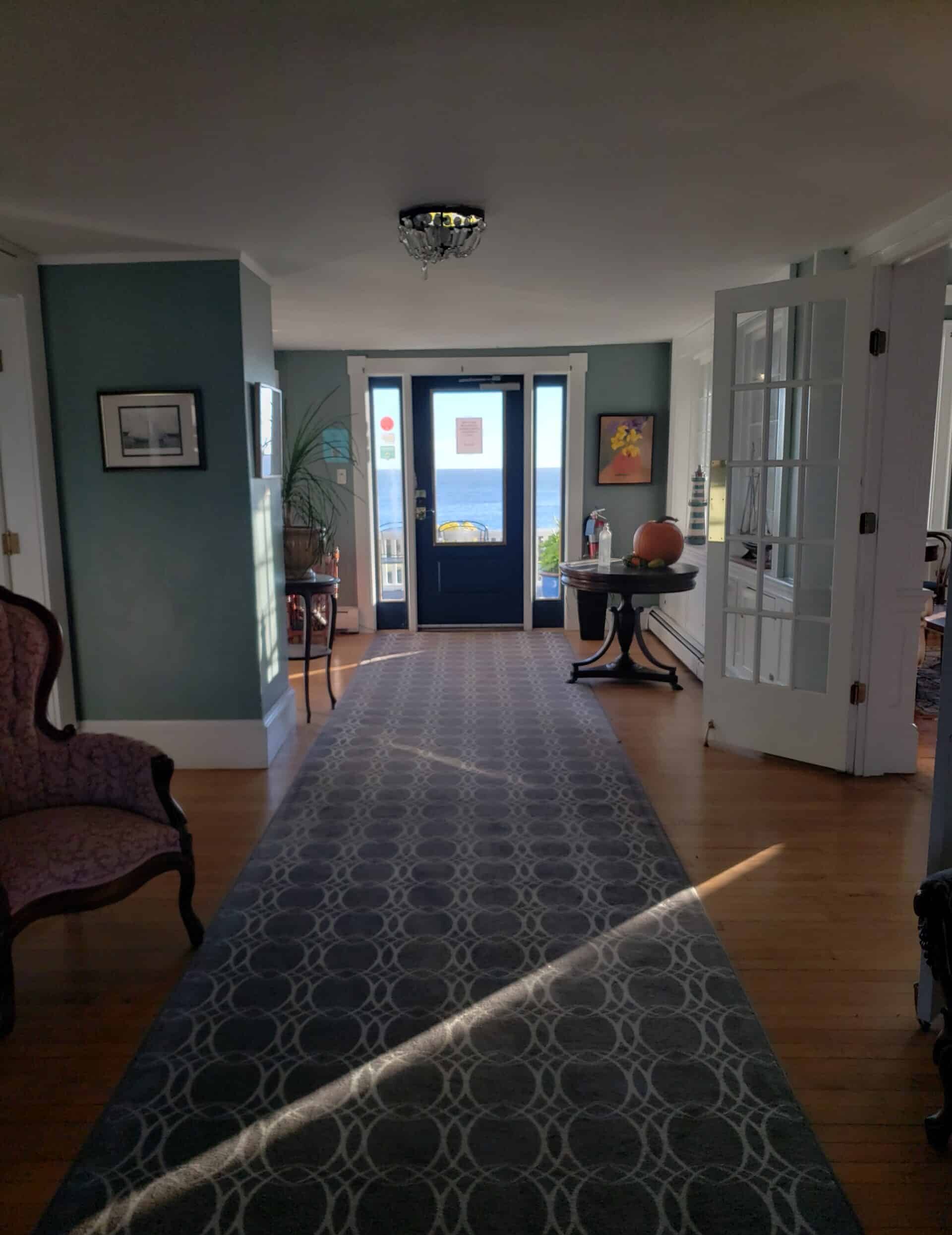 Entrance area to an in with a door that leads to a blue ocean. A blue carpet leads from the doorway.