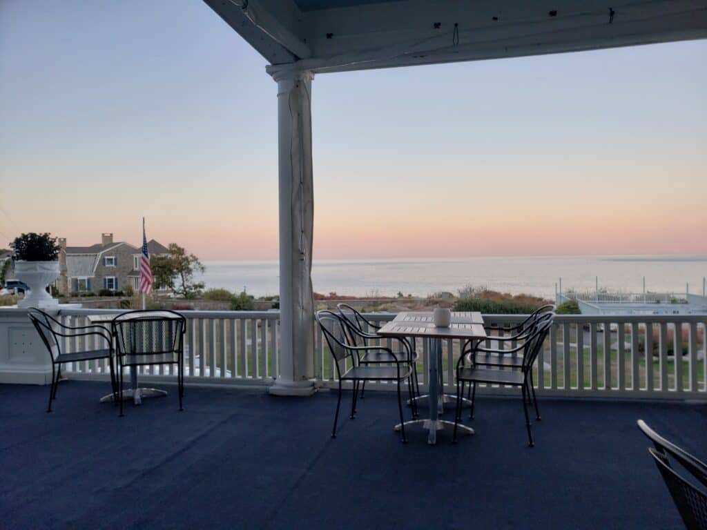 Tables and chairs sitting on a porch overlooking a sunset over the water.