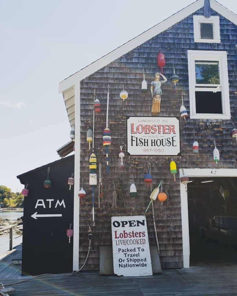 A sign on the side of a grey building that reads \"Lobster Fish House\"