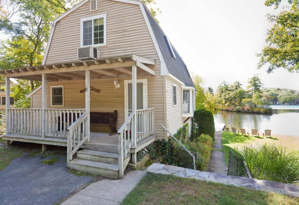 A beige Cape Cod house with a white porch and steps with a white wooden railing on each side. 