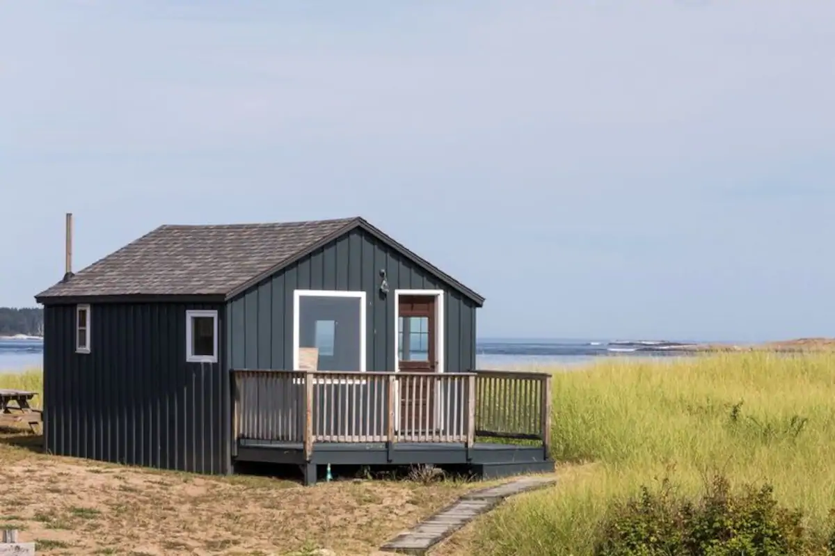 A grey wooden building with a body of water in the background