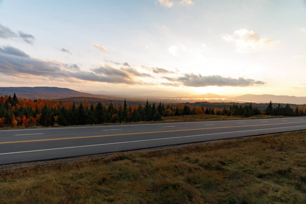 A Maine scenic byway is surrounded by vibrant fall foliage under an early morning sky