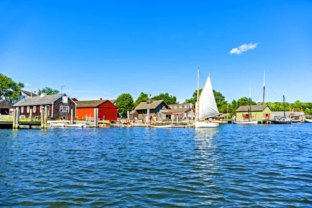 A body of blue water with a white sailboat and some buildings on the shore