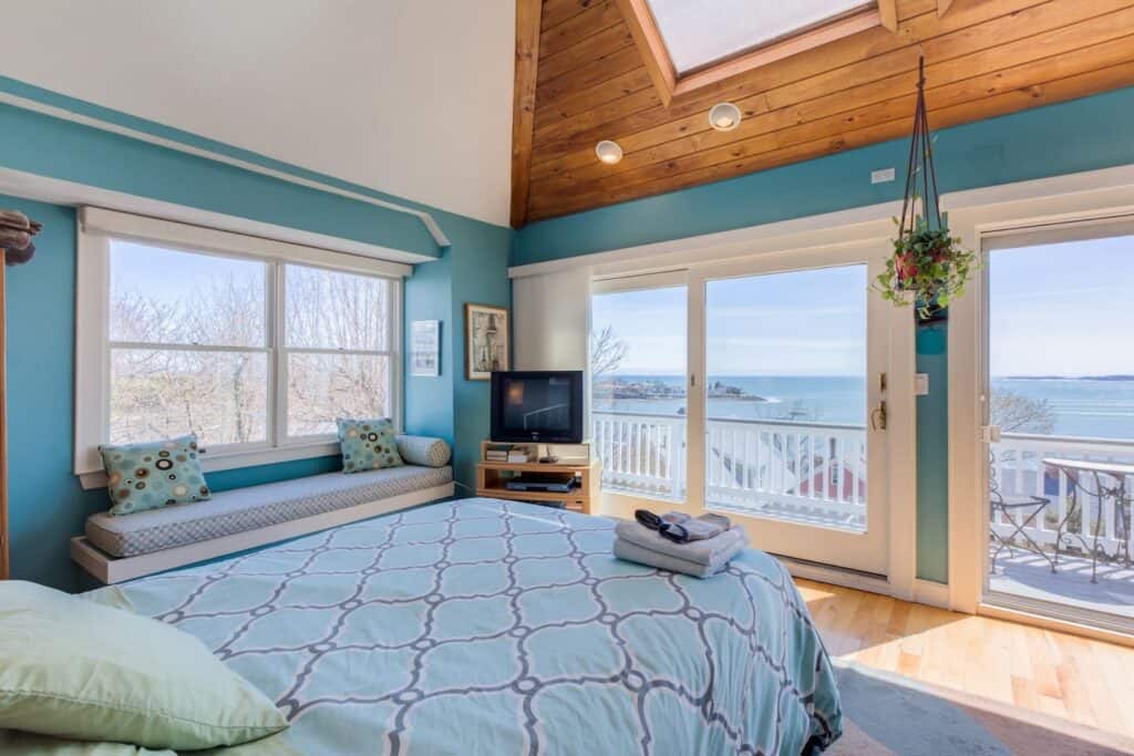 Beautiful hotel room with blue walls and bedspread, and a large sliding door leading out to a balcony overlooking blue water.