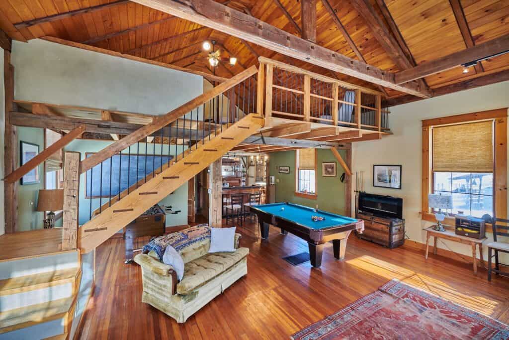 Interior room with a sofa and ping pong table below; a flight of wooden stairs leading up to a loft.