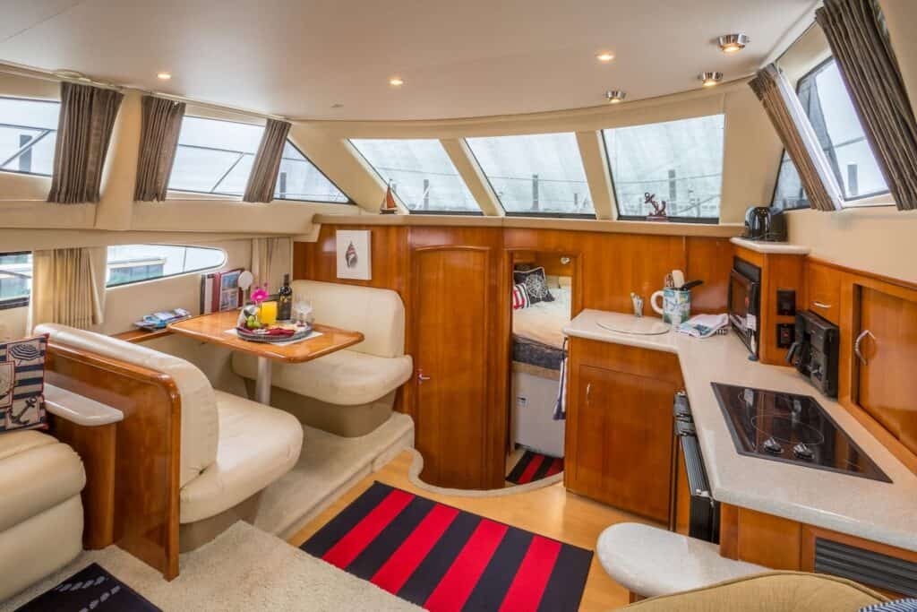 A kitchen area on a yacht, with white leather benches and a navy blue and red striped throw rug.