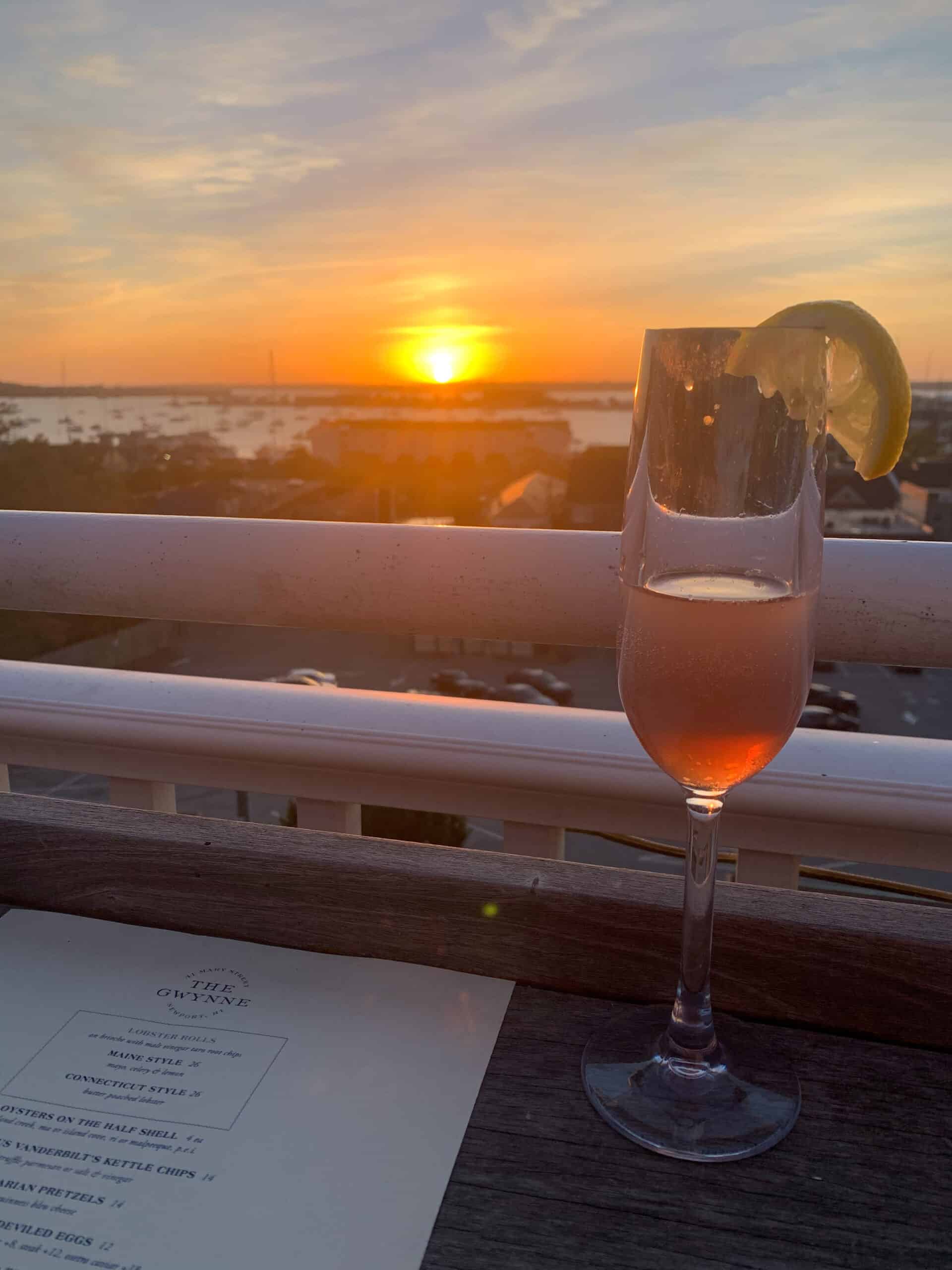 A glass of rose wine on a table in front of a railing with a sunset in the distance