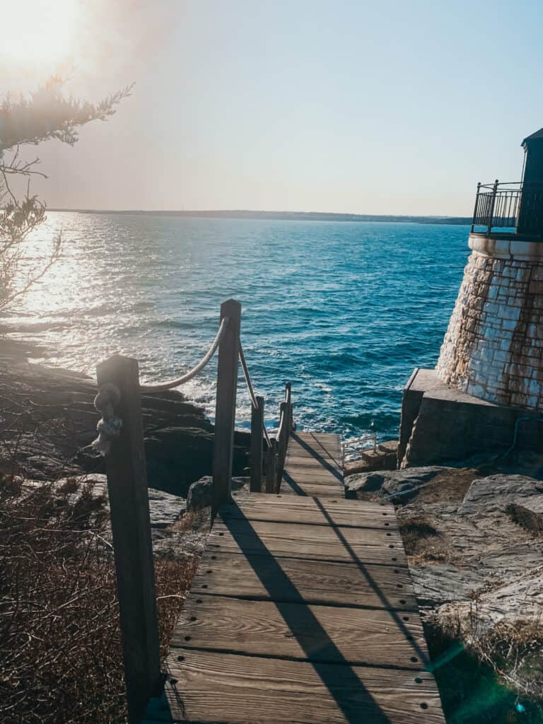 Wooden steps with a rope railing leading down to the blue water next to a tower with a rail around it