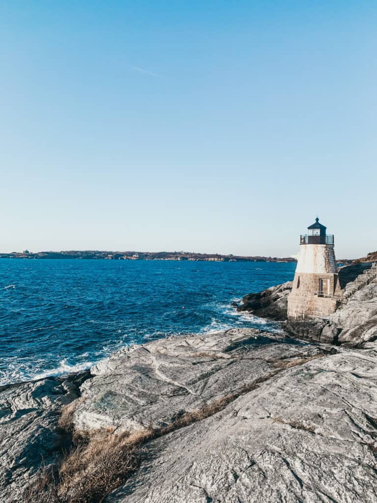 Large body of blue water next to a white lighthouse on the rocky shore