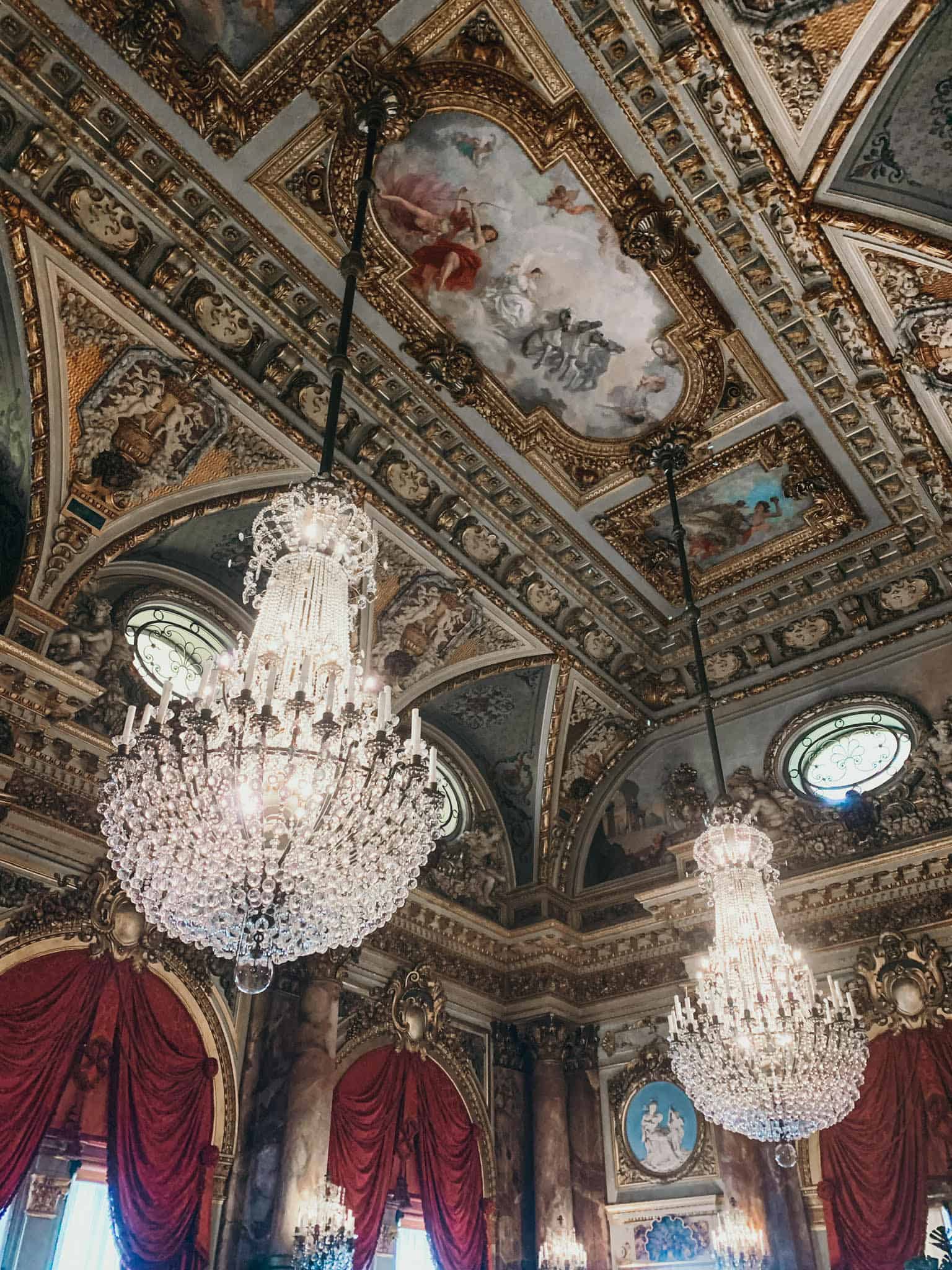 2 crystal chandeliers hanging down from an ornate painted ceiling