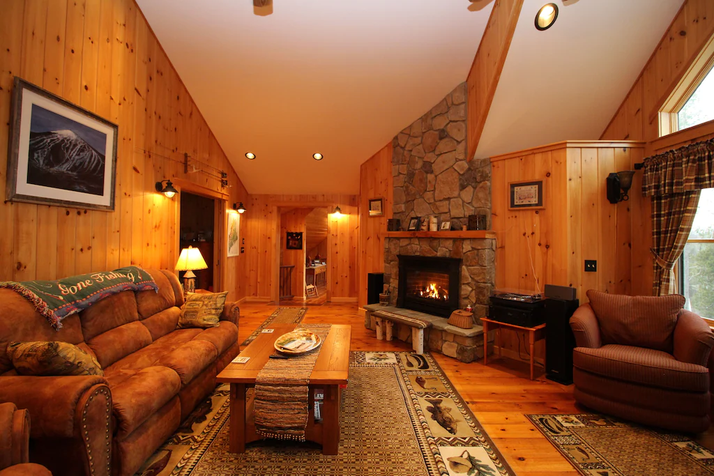 A living room with sofa, coffee table and stone fireplace with fire burning