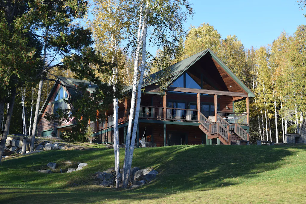 A big chalet with lots of windows facing a lawn and trees