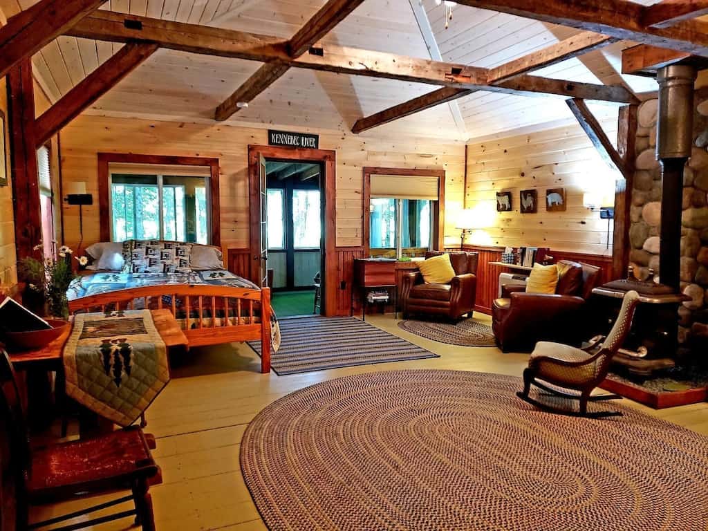 A bedroom with a wooden bed, paneled walls, beams and oval braid rug