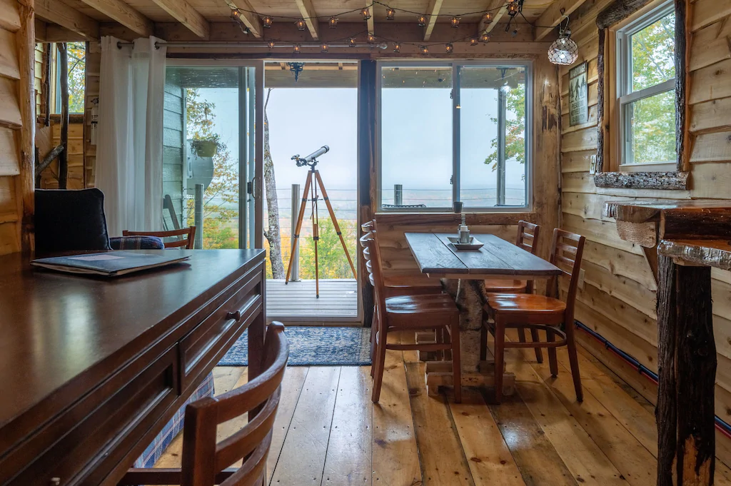 A room with tables and chairs with many windows by the sea and a telescope standing outside the building.