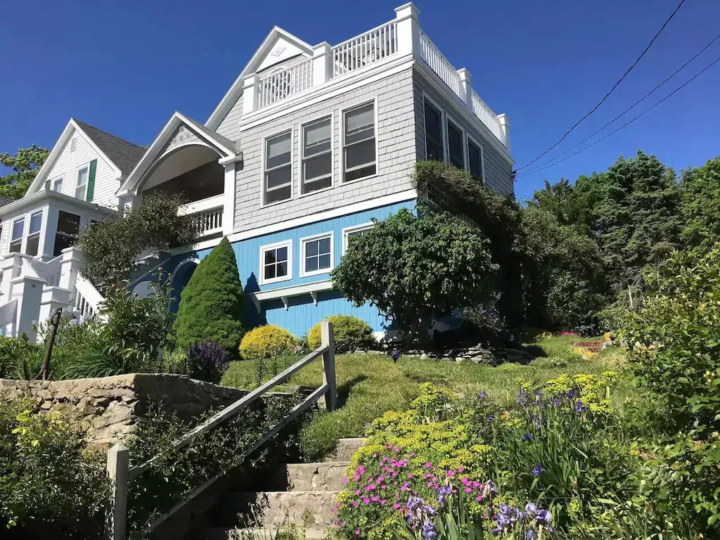 A flight of concrete steps leading to a large house up high on a hill surrounded by shrubbery