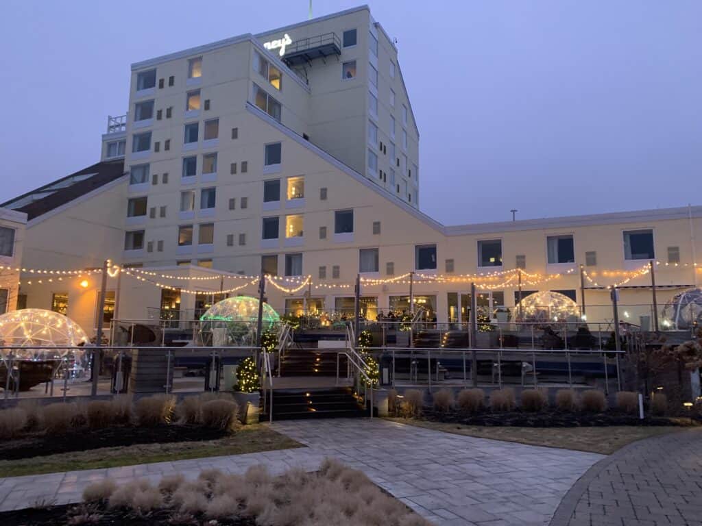 Yellow building under a grey sky with a restaurant on the patio. Bright holiday lights are on the patio.