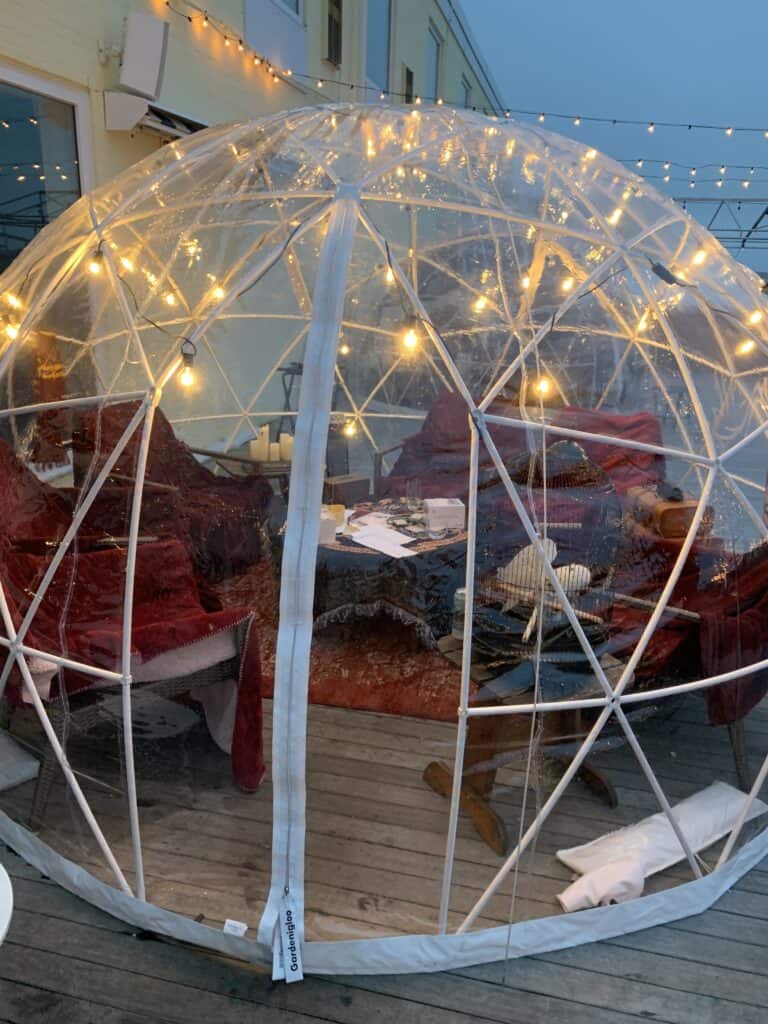 Red chairs in a circular position inside of an outdoor igloo with holiday lights.