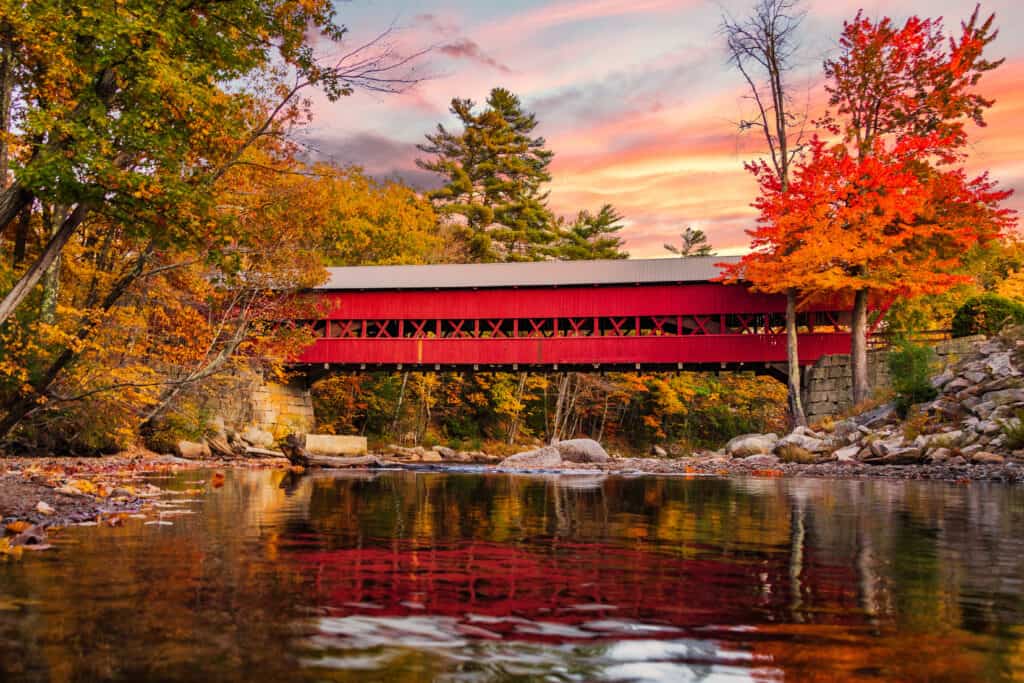 Red covered bridge over a pond under a sunset sky.