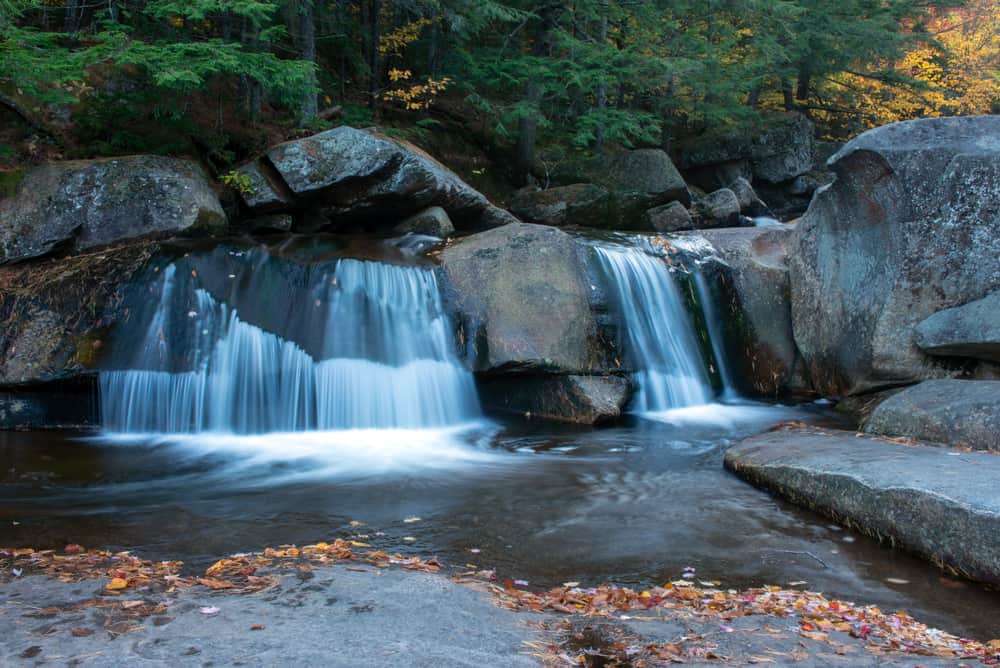 Large waterfall surrounded by slick rock leading into a pond surrounded by forests.