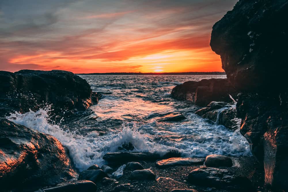 A colorful sunset over a body of water splashing onto rocks