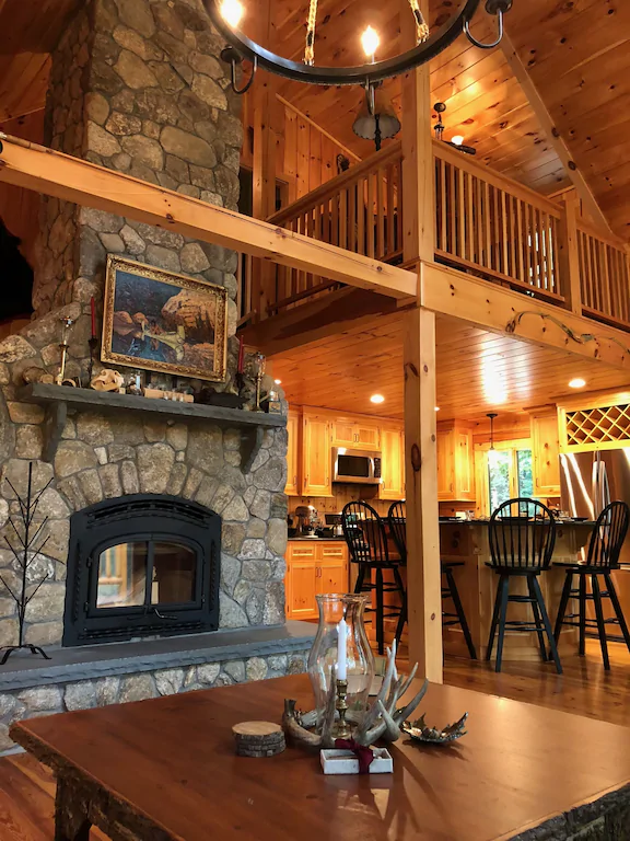 A 2 story chalet with a dining table and stone fireplace
