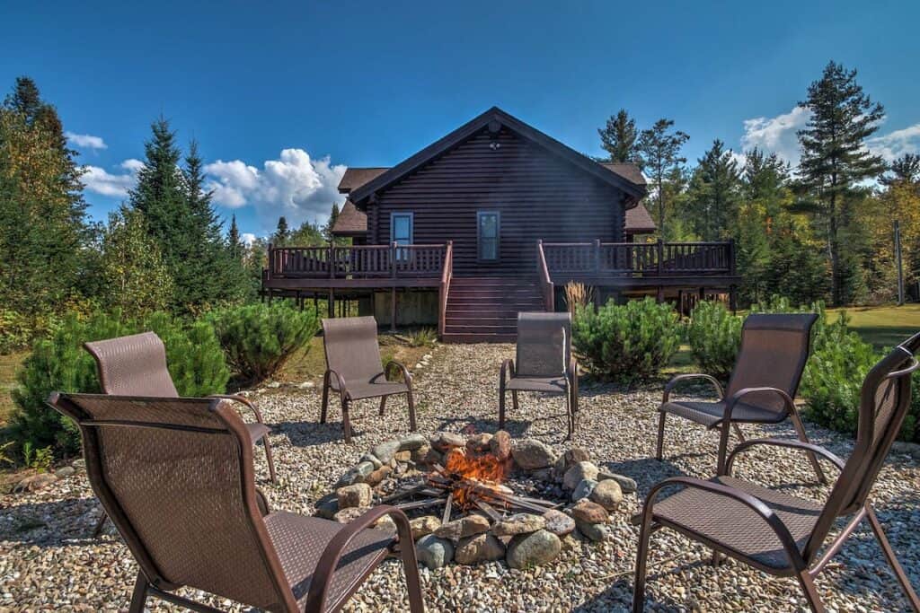 A outdoor fire pit surrounded by chairs with a cabin in the background