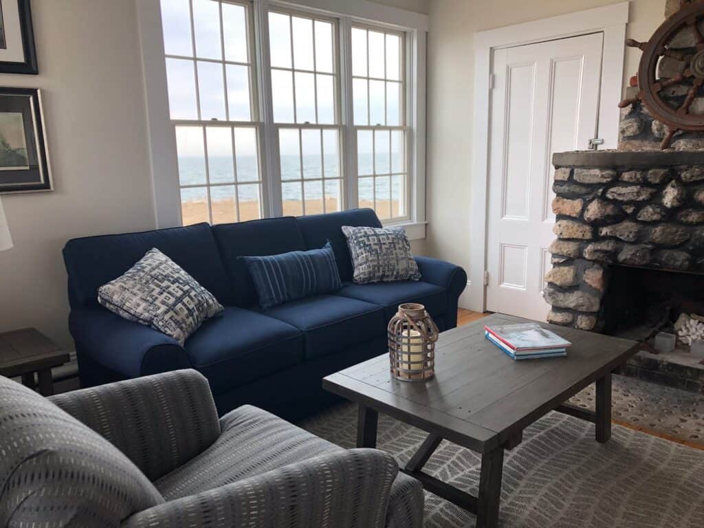 Living room with a window featuring a view of the coast. A blue couch and a grey chair sit around a coffee table.
