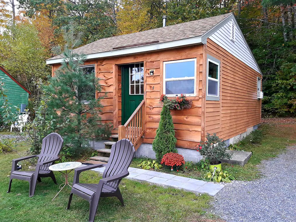 Log cabin with a green door and Adirondack chairs out front