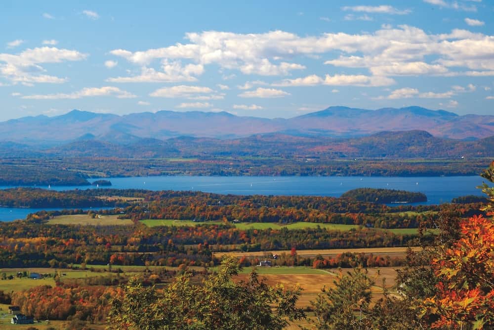 Landscape view of distant mountains and a lake with fall foliage dotting the scene on one of the best hikes near Burlington Vermont.