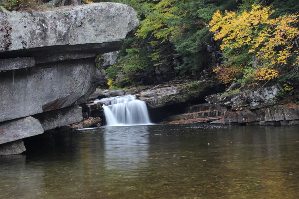 Short waterfall cascading into a pond by fall foliage trees.