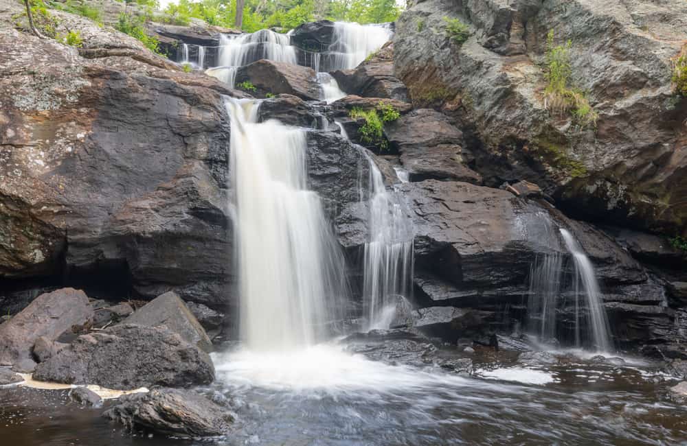Large Connecticut waterfall splits into two and cascades into a body of water.