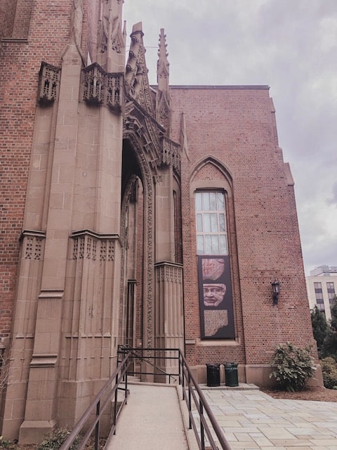 A large brick building with tall Gothic style spires on its entrance on a grey day