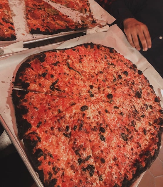A New Haven style apizza is seen on a table with crispy burnt edges and tomato sauce on top