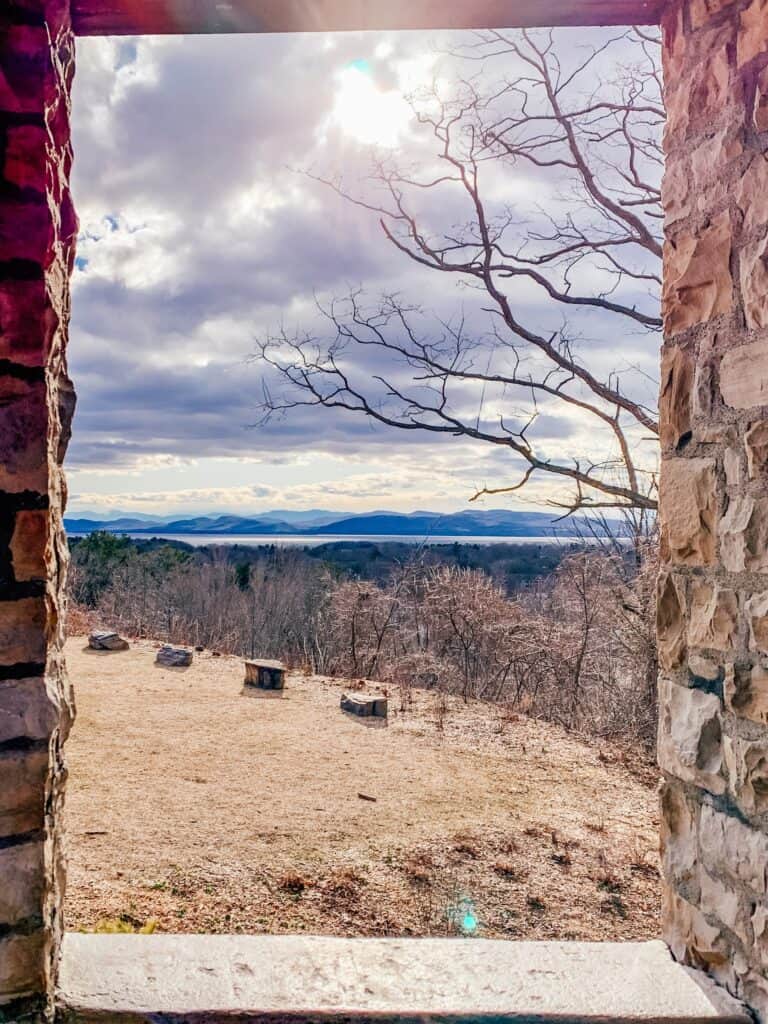 View between two stone columns of blue mountains and a lake in the distance under a cloudy sky.