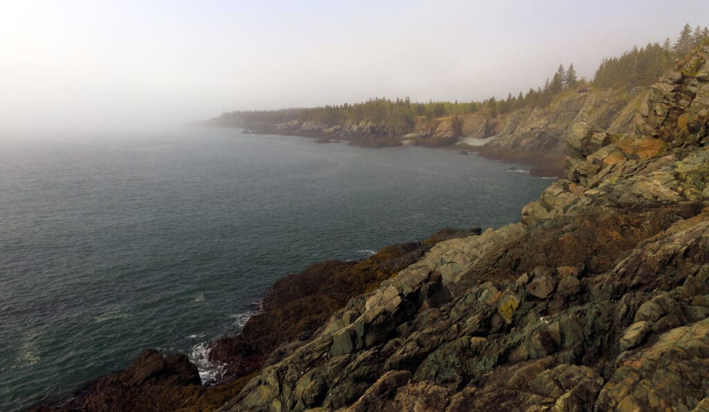 Foggy view of a rocky coastline with blue waters.