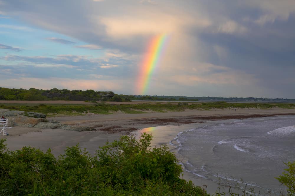 View of a rainbow coming through the clouds down to the beach.