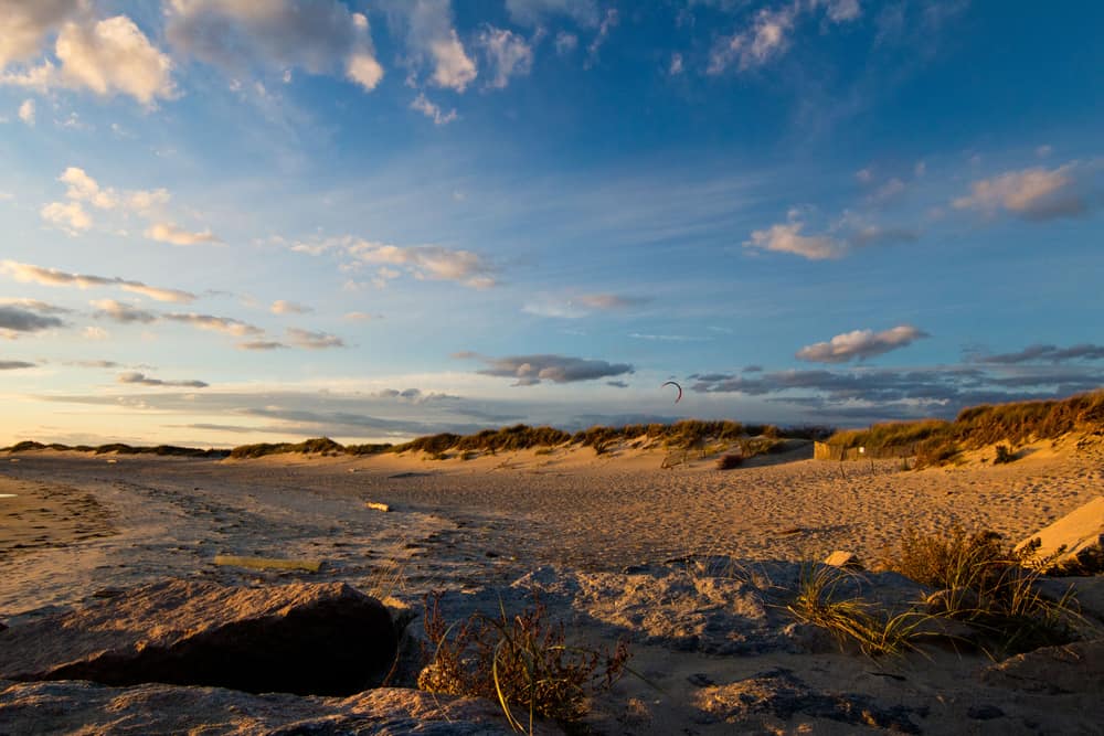 Sandy landscape with greenery under a blue cloudy sky at a popular Rhode Island beach.