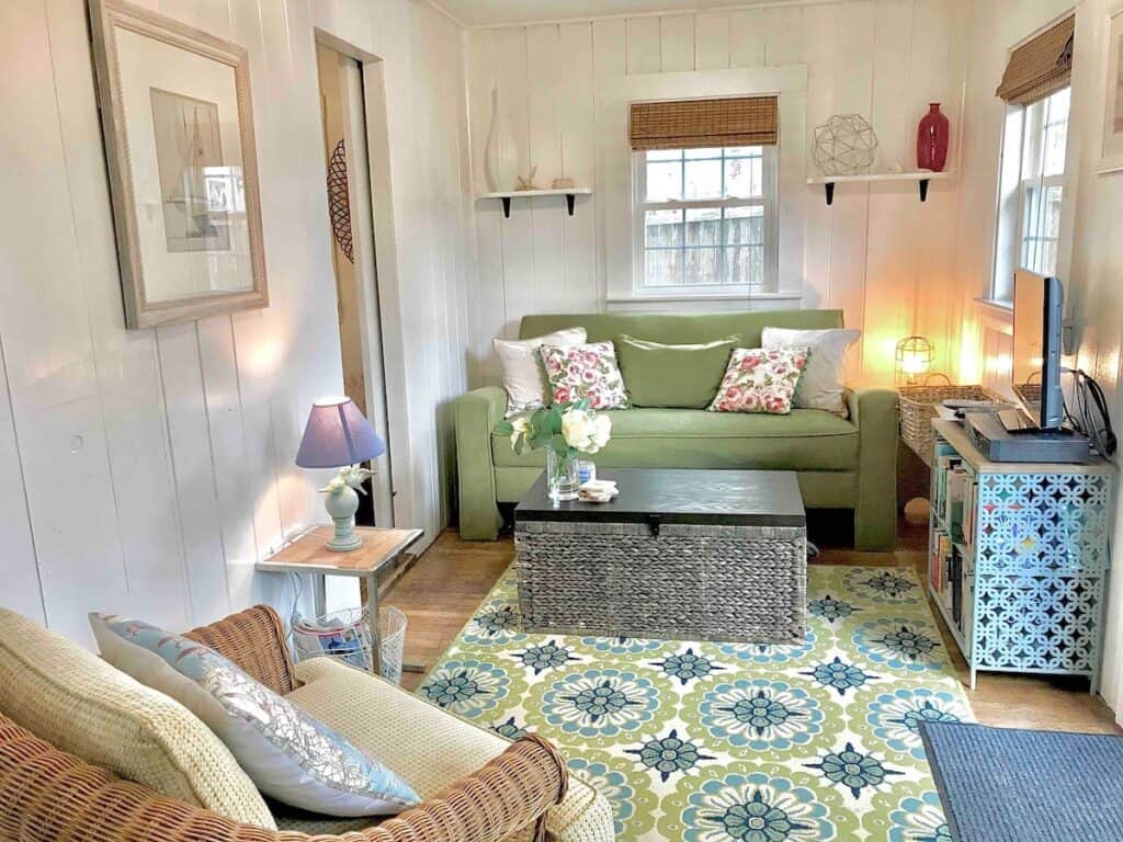 Interior of a living room in a home with white walls. The theme of the room is green and blue. A green couch sits against the wall with a coffee table next to it.