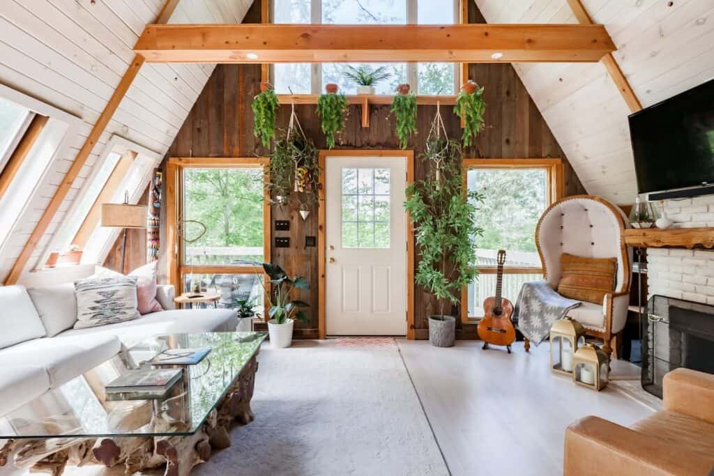 Interior of a living room with brown walls and high ceilings. To the left, a white couch is sitting next to a coffee table. On the right is a white chair with a guitar next to it.