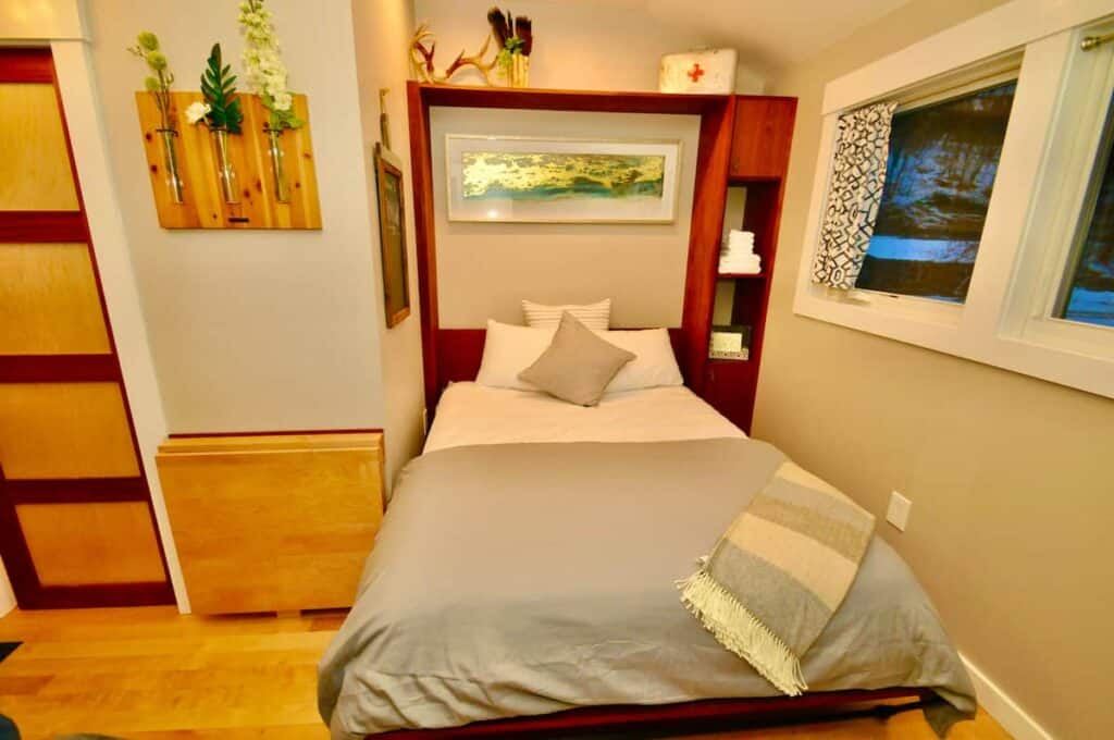 Bed with grey bedding made inside a bedroom. A piece of art sits above the bed with a green design. To the right of the bed is a window showing the darkness of night.