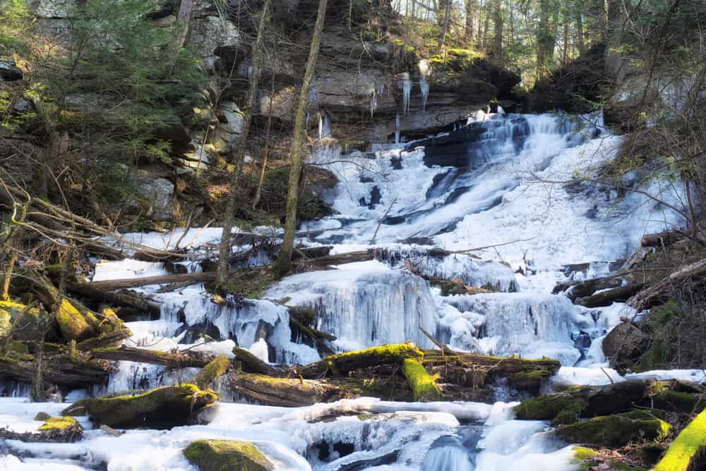 Connecticut waterfalls are frozen in their tracks over rocks and trees.
